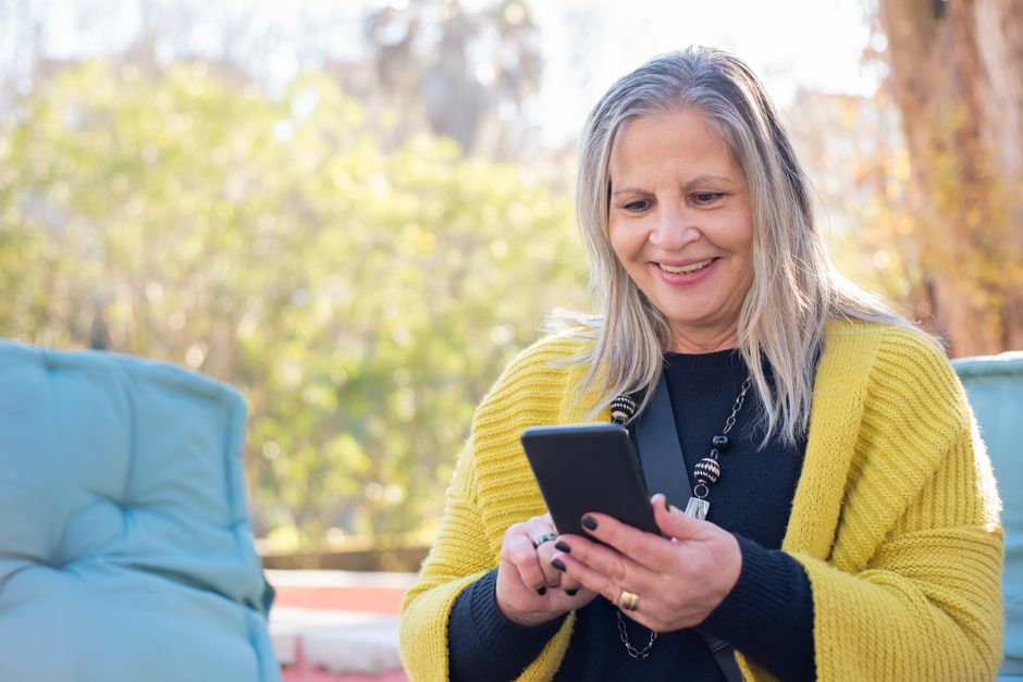 elderly woman smiling using smartphone outdoors