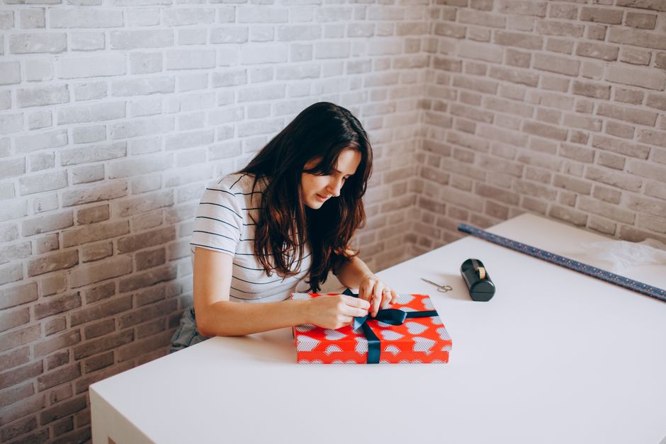 person wrapping gift box at home table